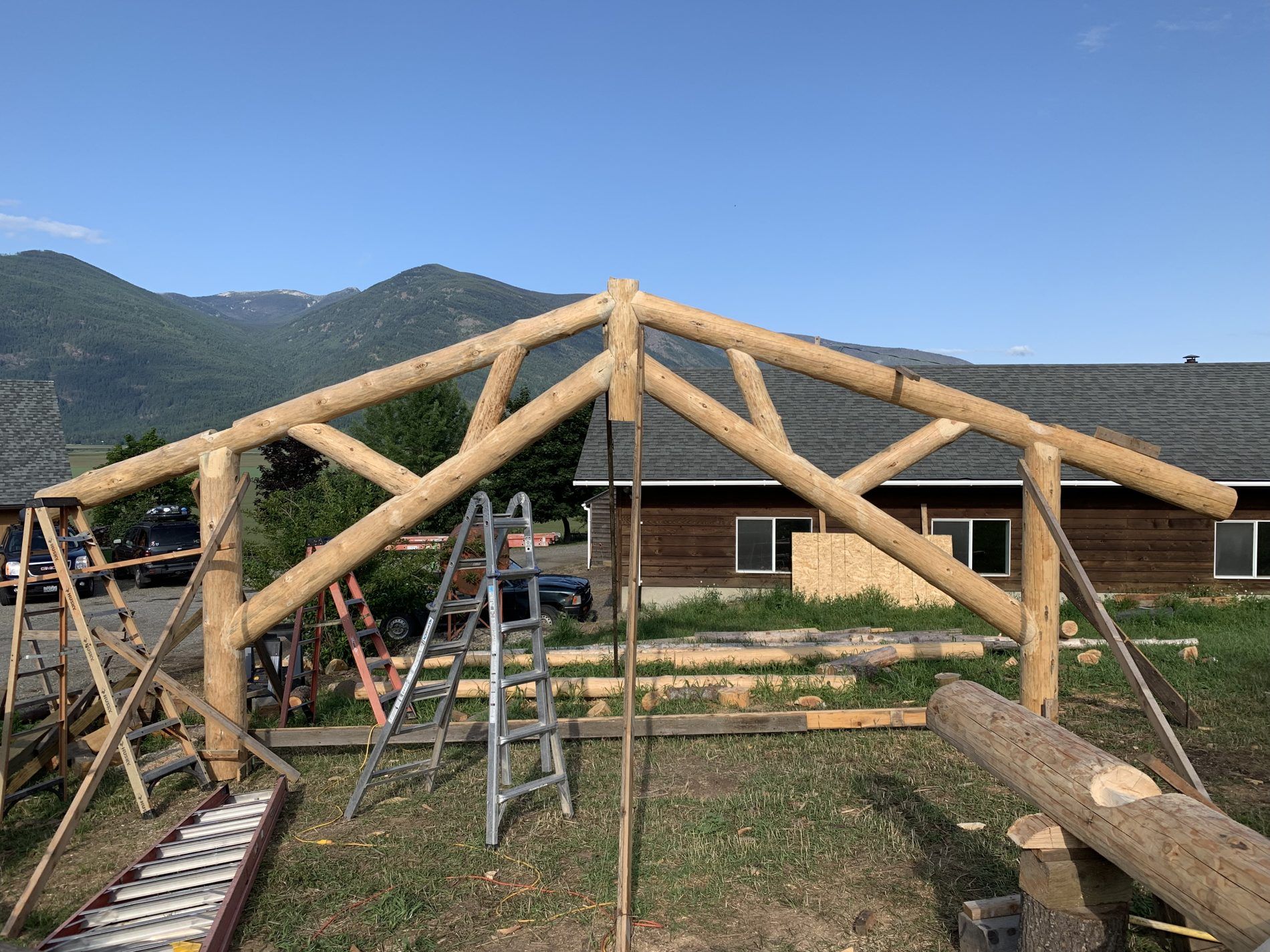 A reverse scissor log truss set in place over a log home, scaffolding still standing