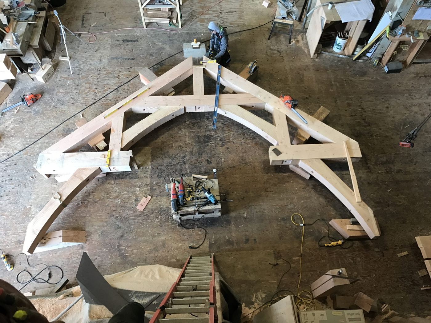 A large curved timber truss laid out full-size on a shop floor